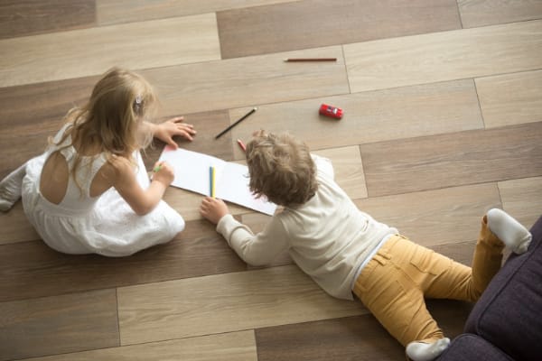 Two children sitting on a wood floor, drawing.